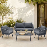 Outdoor patio set with gray sofa and chairs on a patio with plants and a building in the background.